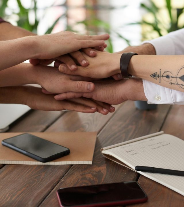 pexels-photo-3184431-3184431 Hands from a diverse team stack on a table symbolizing unity and teamwork in a modern office setting.